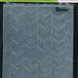 May include: A clear embossing folder with a repeating chevron pattern. The folder is 4.25 inches by 5.75 inches (10.7cm x 14.6cm) and features the "Darice" brand name. The package also includes the words "Embossing Essentials".