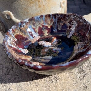 May include: A small, dark brown ceramic bowl with a white and brown glaze. The bowl has a textured, uneven surface and a slightly rounded shape.