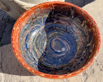 May include: A ceramic bowl with a swirling blue and brown glaze. The bowl has a red rim with a white pattern.