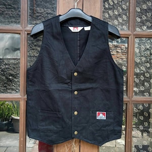 May include: A black denim waistcoat with a button fastening and two front pockets. The waistcoat has a red and white logo patch that says "Ben Davis" on the right pocket.