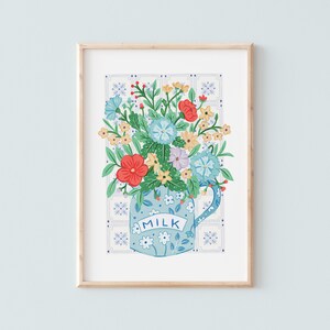 Puede incluir: Una taza de cerámica azul con una etiqueta blanca "MILK", llena de un ramo de flores de colores, incluyendo flores rojas, amarillas, azules y moradas. La taza está sobre un fondo blanco con un patrón de azulejos azules y blancos.