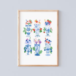 Puede incluir: Una impresión enmarcada que presenta seis batidos ilustrados en vasos con diseños florales azules y blancos. Cada batido está cubierto con diferentes frutas y adornos, incluyendo sandía, cerezas y fresas. La obra de arte tiene un aspecto caprichoso y vintage.