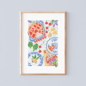 Puede incluir: Una impresión enmarcada que muestra una vista superior de una mesa puesta. La imagen incluye una tarta, cerezas, alcachofas, pasta y platos. También se ve un paquete de "La Cucina".