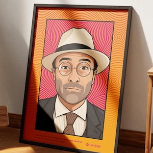 Può includere: Ritratto incorniciato di un uomo con un fedora e occhiali, su uno sfondo rosa e arancione con cerchi concentrici. L'opera d'arte è in una cornice nera e si appoggia a un muro bianco. Una sedia e un tavolino in legno sono in primo piano.