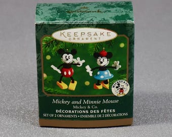 May include: A green box featuring a Mickey and Minnie Mouse Keepsake Ornament set. The box has the text "Mickey and Minnie Mouse" and "Set of 2 Ornaments". The ornaments are cartoon figures of Mickey and Minnie Mouse.