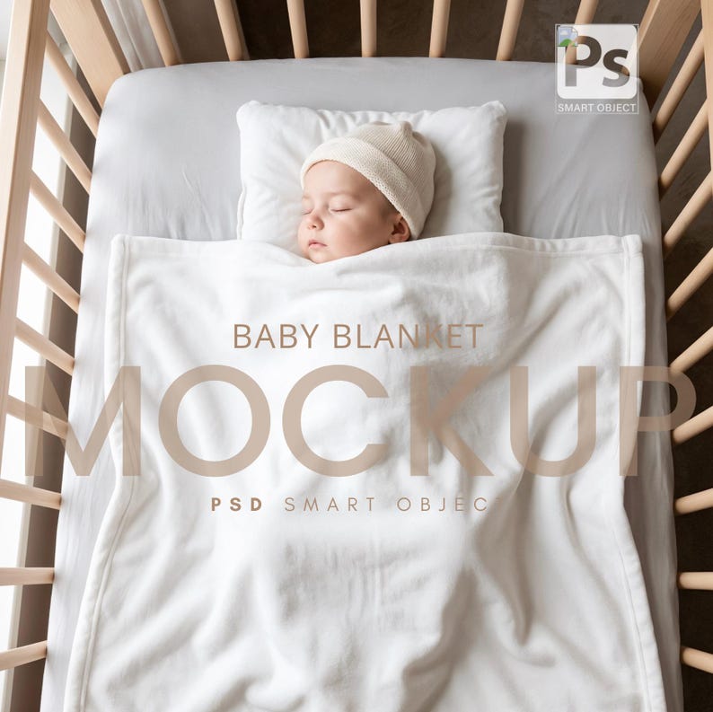 May include: A sleeping baby wearing a beige knit cap rests on a white pillow and is covered by a white baby blanket in a wooden crib. The blanket has the words "BABY BLANKET MOCKUP" printed on it.