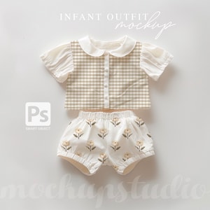 May include: A white baby outfit with a gingham top and floral print shorts. The top has a white collar and short sleeves. The shorts have an elastic waistband and a ruffled hem.