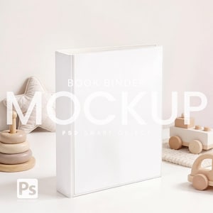 以下が含まれることがあります： 前面に「MOCKUP」という文字が重ねられた白いブックバインダーのモックアップ。バインダーは白い表面にあり、背景には木製のおもちゃと星型の枕があります。「BOOK BINDER」と「PSD SMART OBJECT」の文字も表示されています。