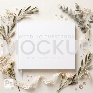 Può includere: Un mockup di libro degli ospiti di nozze bianco con il testo "WEDDING GUESTBOOK MOCKUP" in grigio. Il libro è circondato da elementi floreali, tra cui rami di ulivo, rose e nastro di pizzo. Piccole perle e bottoni sono sparsi.