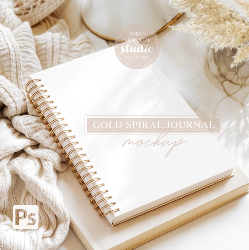 May include: A white spiral bound journal with gold rings, lying on top of a beige book. The journal is blank and ready for writing. The text "GOLD SPIRAL JOURNAL MOCKUP" is printed on the journal.
