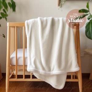 May include: White plush blanket draped over a wooden crib with a white mattress. The crib is in a room with a plant in a woven basket and a wooden side table.