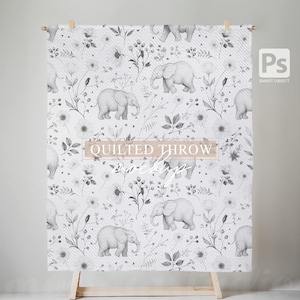 Könnte beinhalten: Eine weiße gesteppte Wurfdecke mit einem grauen Blumen- und Elefantenmuster. Der Text "QUILTED THROW" ist auf der Decke aufgedruckt.