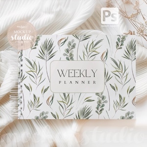 May include: A white weekly planner with a green and brown floral pattern. The planner has a spiral binding and the words "Weekly Planner" are printed on the front cover.