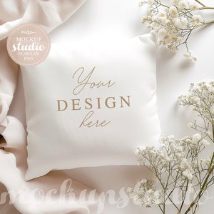 Puede incluir: Almohada cuadrada blanca con el texto "Your DESIGN here" sobre un fondo blanco con flores blancas y un trozo de tela beige.