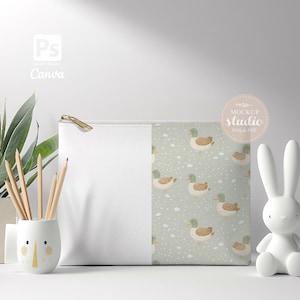 May include: A white zippered pouch with a green and white duck pattern on one side. The pouch is sitting on a white surface with a white ceramic pencil holder and a white ceramic bunny.