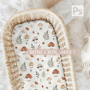 May include: A white mini crib sheet with a mushroom and leaf pattern. The sheet is in a wicker basket.