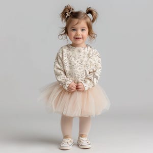 May include: A young girl wearing a cream-colored sweatshirt with a floral and giraffe print, a tulle tutu skirt, and white sneakers.
