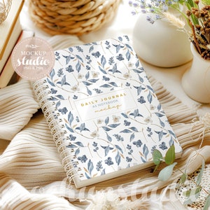 May include: A white spiral bound journal with a blue and white floral pattern. The cover has the text "Daily Journal as Notebook mockup" printed on it.