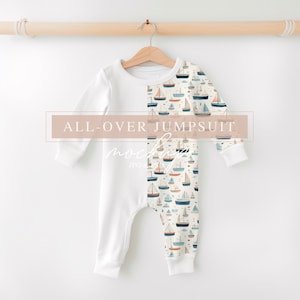 May include: A white long-sleeved baby onesie with a sailboat print on the right side. The onesie is hanging on a wooden hanger against a white background. The text "ALL-OVER JUMPSUIT MOCKUP JPG & PSD" is displayed on the image.