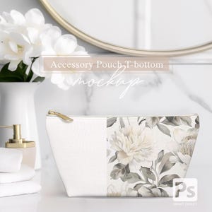 May include: A white zippered pouch with a floral design on the right side. The pouch is sitting on a white marble surface. The text "Accessory Pouch T-bottom mockup" is written in white on a transparent background.