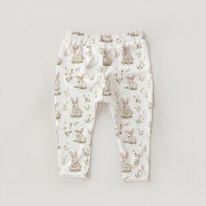 Peut inclure: Pantalon de b&eacute;b&eacute; blanc avec un motif int&eacute;gral de lapins &agrave; l'aquarelle et de petites fleurs jaunes. Le pantalon a une taille &eacute;lastique et une apparence douce, adapt&eacute; aux nourrissons et aux tout-petits.