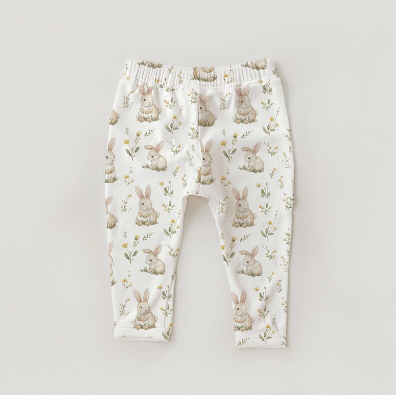 Peut inclure: Pantalon de b&eacute;b&eacute; blanc avec un motif int&eacute;gral de lapins &agrave; l'aquarelle et de petites fleurs jaunes. Le pantalon a une taille &eacute;lastique et une apparence douce, adapt&eacute; aux nourrissons et aux tout-petits.