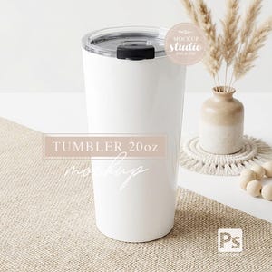 Puede incluir: Un vaso blanco de 20 oz (aproximadamente 590 ml) con tapa negra. El vaso cilíndrico se muestra sobre una superficie de tono neutro. El texto en el vaso dice "TUMBLER 20oz mockup". El fondo incluye un jarrón con plantas secas.
