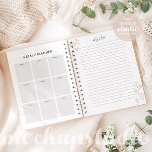 May include: A white weekly planner with a floral design on the cover. The planner has a spiral binding and includes a section for weekly planning and a notes section. The planner is open to the weekly planning section, which is blank.