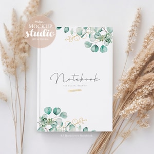 May include: A white A5 hardcover notebook mockup featuring a green and gold eucalyptus design. The text "Notebook" and "PSD DIGITAL MOCK-UP" is printed on the front cover.
