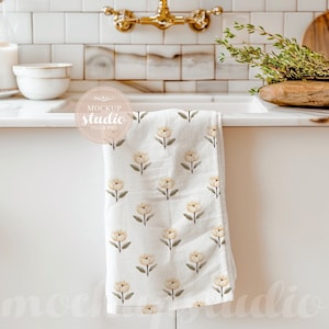 Puede incluir: Una toalla de cocina blanca con un patrón floral de pequeñas flores amarillas colgando de un armario blanco. La toalla está hecha de un material suave y absorbente, perfecto para secar platos o manos.