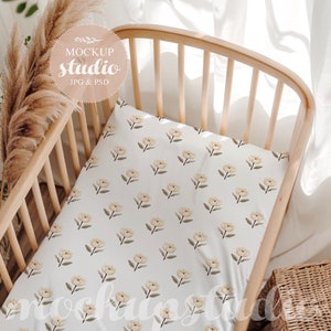 May include: A white crib sheet with a floral pattern of yellow flowers and green leaves. The sheet is in a wooden crib with a white background.
