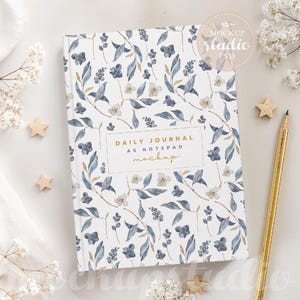 May include: A white journal with a blue and gold floral pattern. The cover has the text "Daily Journal as Notepad Mockup" in gold lettering.