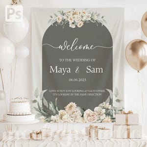 K&ouml;nnte beinhalten: Ein Hochzeits-Willkommensschild mit dem Text "welcome" und den Namen "Maya & Sam" mit dem Datum 08.06.2023. Das Schild ist mit Blumenarrangements und einem Zitat verziert. Wei&szlig;e und goldene Luftballons und eine Torte sind ebenfalls zu sehen.