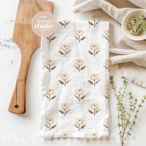 May include: A white kitchen towel with a floral pattern of beige flowers. The towel is folded and lying on a white marble surface. There is a wooden chopping board and a small bowl with green herbs in the background.