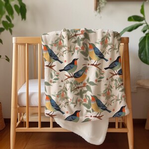 May include: A white and cream throw blanket with a colorful bird pattern. The blanket features a variety of birds with blue, green, yellow, and orange accents. The birds are perched on branches with green leaves and red berries.