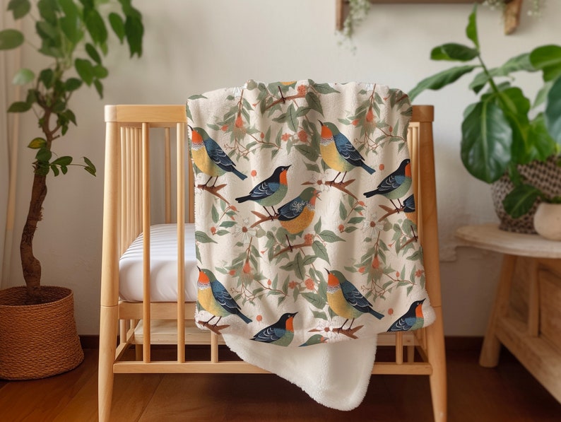 May include: A white and cream throw blanket with a colorful bird pattern. The blanket features a variety of birds with blue, green, yellow, and orange accents. The birds are perched on branches with green leaves and red berries.