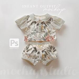 May include: A two-piece baby outfit with a floral print. The top has a peter pan collar and short sleeves. The shorts are bloomers with a ruffled hem. The outfit is in shades of green, white, and pink.