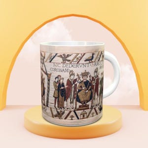 May include: A white ceramic mug featuring a detailed historical illustration of a coronation scene. The print includes Latin text that reads HIC DEDERVNT HAROLDO CORONAM REGIS, depicting figures in medieval robes, a seated monarch, and birds.