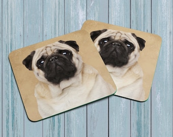 May include: Two square coasters with a beige background and a picture of a pug dog on each. The pug has a light brown and white coat and is looking directly at the camera.