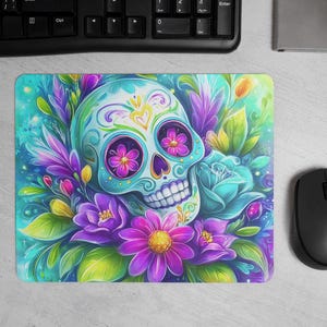 Peut inclure: Tapis de souris vibrant avec un motif de crâne de sucre. Le crâne est orné de motifs floraux et entouré de fleurs violettes, roses et bleues. Le fond est un mélange de teintes turquoise et vertes, créant une esthétique colorée et artistique.