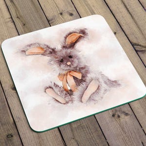 May include: A watercolor illustration of a brown bunny rabbit with a peach-colored bow. The bunny is sitting on a white background with a light pink watercolor wash.