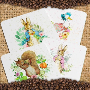 May include: Four illustrated cards featuring Peter Rabbit, a squirrel, a duck, and another Peter Rabbit. The cards are white with a light pink and green floral background. The cards are arranged in a square shape.