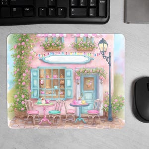 Pode incluir: Ilustração em aquarela de um café rosa com porta e janelas azuis, adornado com flores e um lampião. A cena inclui pequenas mesas e cadeiras, criando uma atmosfera charmosa e convidativa. Um mousepad com uma cena de café.