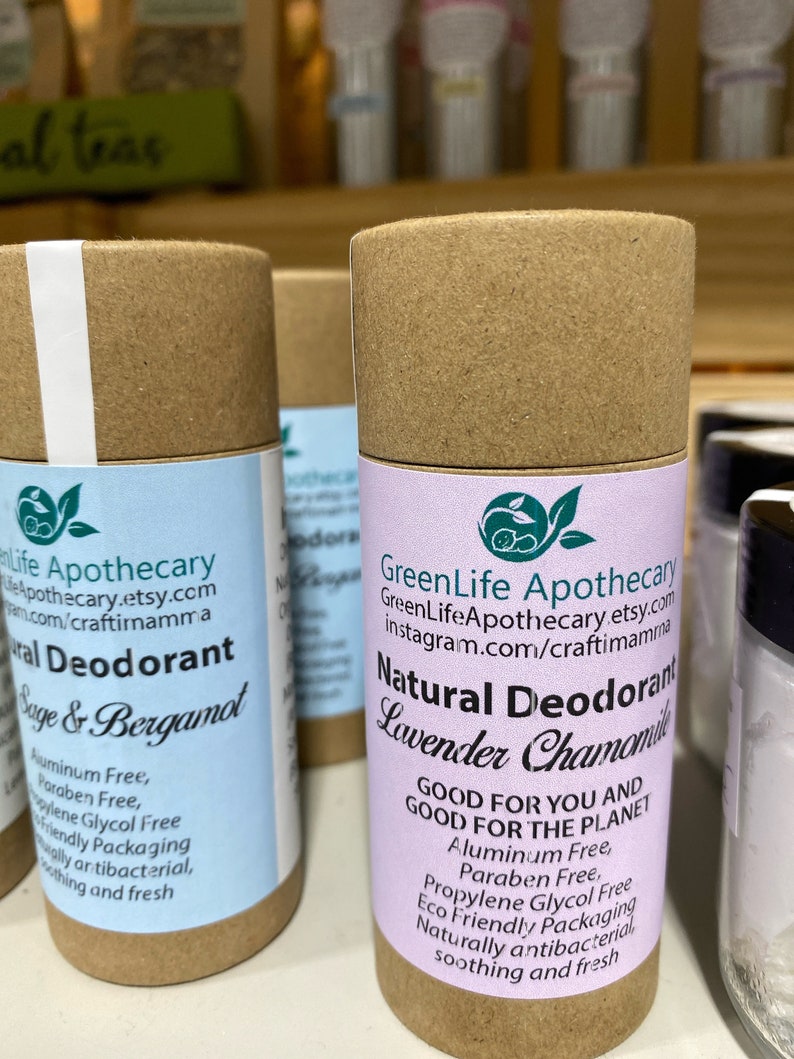 Op de afbeelding: Een bruine kartonnen buis met een wit etiket waarop "GreenLife Apothecary" en "Natuurlijke Deodorant Lavendel Kamille" staat. Het etiket vermeldt ook "Goed voor jou en goed voor de planeet" en somt de ingredi&euml;nten op: "Aluminiumvrij, parabenenvrij, propylenglycolvrij, milieuvriendelijke verpakking, natuurlijk antibacterieel, verzachtend en fris".