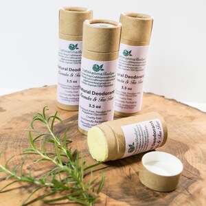 Op de afbeelding: Drie bruine kartonnen buizen met natuurlijke deodorant met lavendel- en theeboomolie. De buizen zijn gelabeld met "Natural Deodorant Lavender & Tea Tree" en vermelden de ingredi&euml;nten, waaronder "Aluminiumvrij, Parabenvrij, Propylenglycolvrij, Milieuvriendelijke verpakking, Dierproefvrij, Natuurlijk antibacterieel, Kalmerend en fris". De buizen zijn elk 3,5 oz.