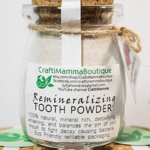 May include: A glass jar with a cork lid filled with white powder. The label reads "Remineralizing Tooth Powder" and includes information about the product, such as "100% natural, mineral rich, detoxifying, whitening, and balances the pH of your mouth to fight decay causing bacteria. Eco Friendly refillable packaging."