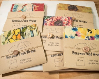 May include: A set of five brown paper packages containing beeswax food wraps. Each package features a different patterned fabric wrap and includes the text "Beeswax Food Wraps" and the size "14"x"14".