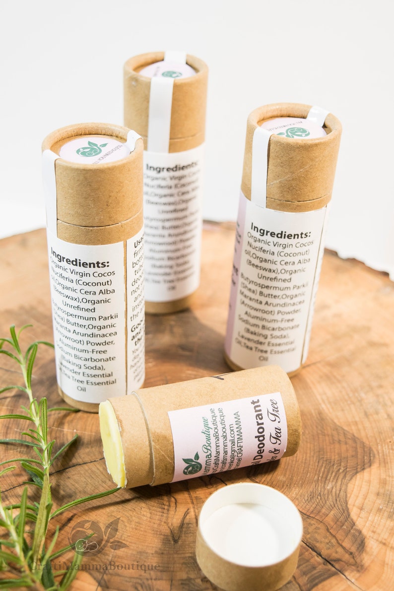 Op de afbeelding: Drie bruine kartonnen buizen met witte etiketten die natuurlijke deodorant bevatten. De etiketten vermelden de ingredi&euml;nten, waaronder biologische kokosolie, sheaboter en tea tree etherische olie. De buizen staan op een houten oppervlak met een takje rozemarijn.