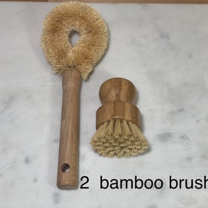 May include: Two bamboo brushes, one with a long handle and a round brush head, and the other with a shorter handle and a round brush head. The brushes are on a white marble surface.