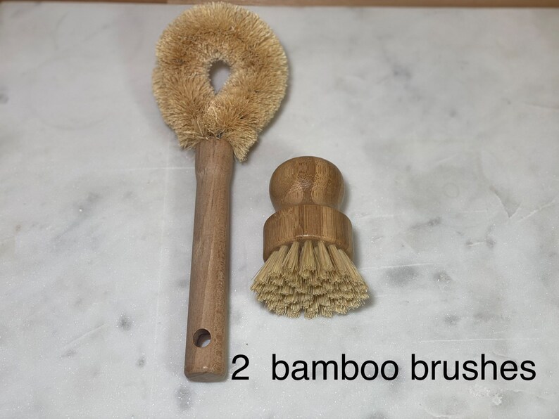 May include: Two bamboo brushes, one with a long handle and a round brush head, and the other with a shorter handle and a round brush head. The brushes are on a white marble surface.
